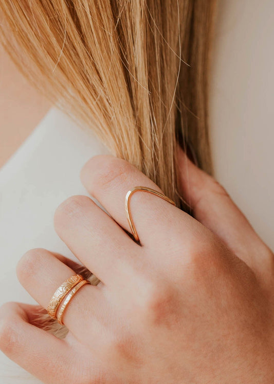 Close-up of a hand with gold rings holding blonde hair, wearing a white top.
