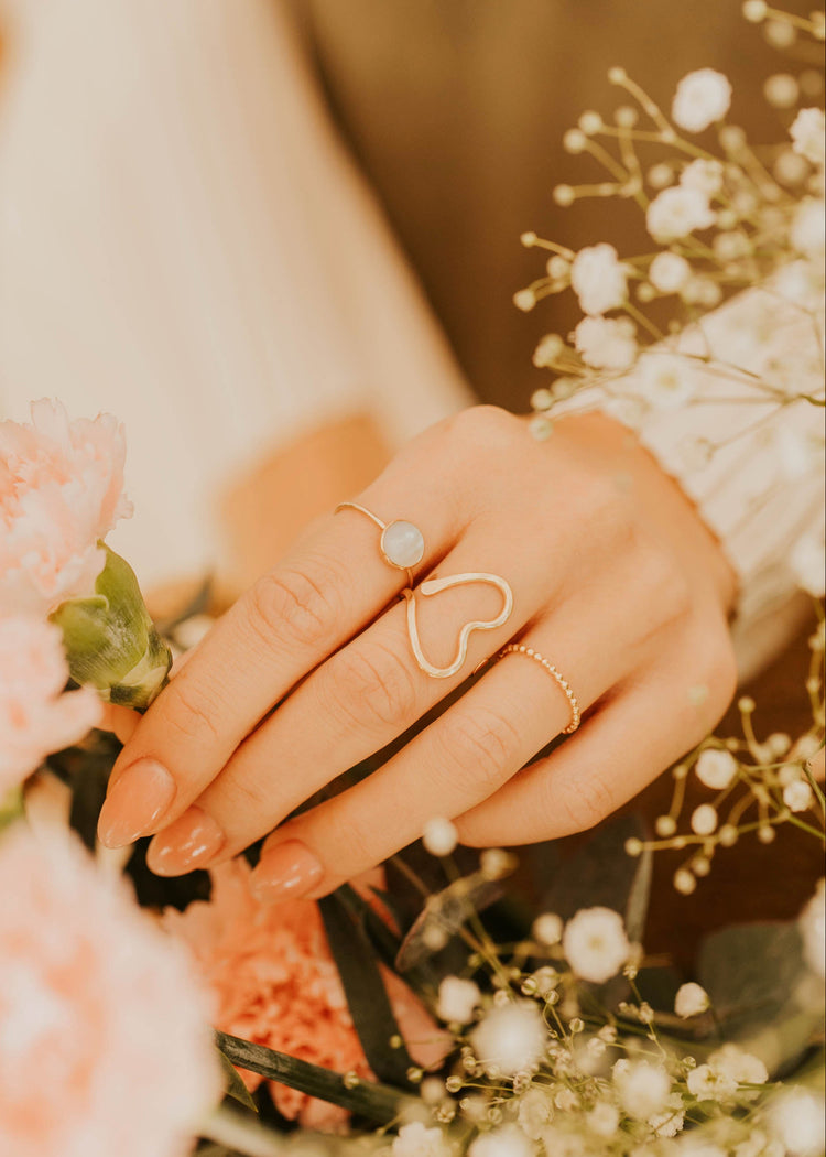 Hand with a heart-shaped ring holding flowers with a blurred background