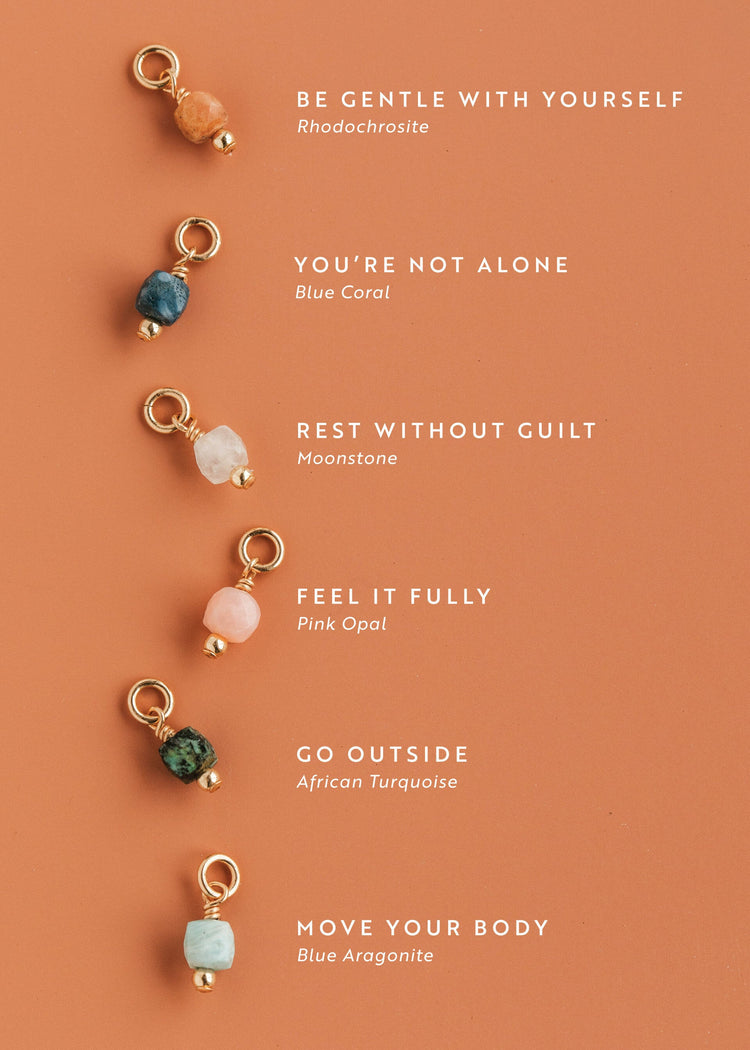 Set of Hello Adorn gemstone charms on a peach background with motivational mental health necklace phrases.