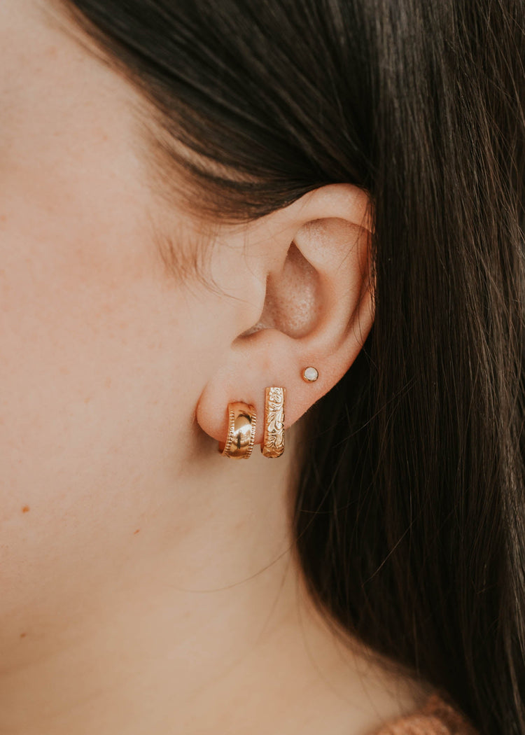 Close-up of an ear wearing gold hoop earrings with a blurred background