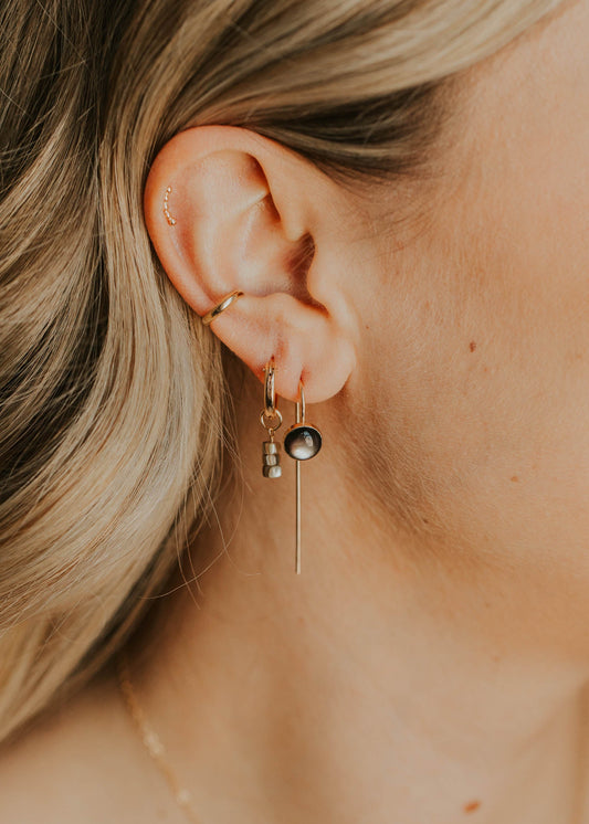 Close-up of an ear wearing a gold earring with a small round pendant.