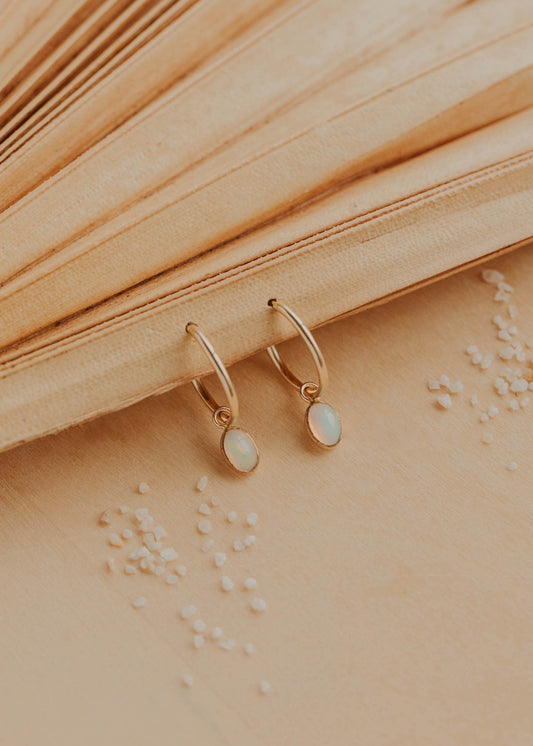 Gold hoop earrings with opal stones on a textured beige surface