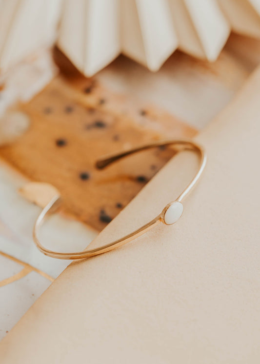 Gold bracelet on a textured beige surface with a blurred background