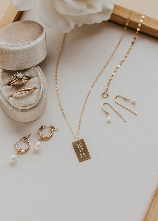 Gold jewelry including a necklace, earrings, and rings on a light surface with a white flower.