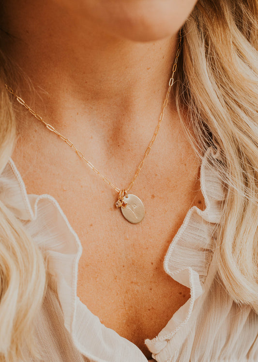 Close-up of a person wearing a delicate gold necklace with a round pendant.