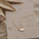 A pendant necklace with a hammered disc attached to a dainty chain necklace to create the Supermoon Necklace by Hello Adorn, a moon necklace with a gold disc necklace.