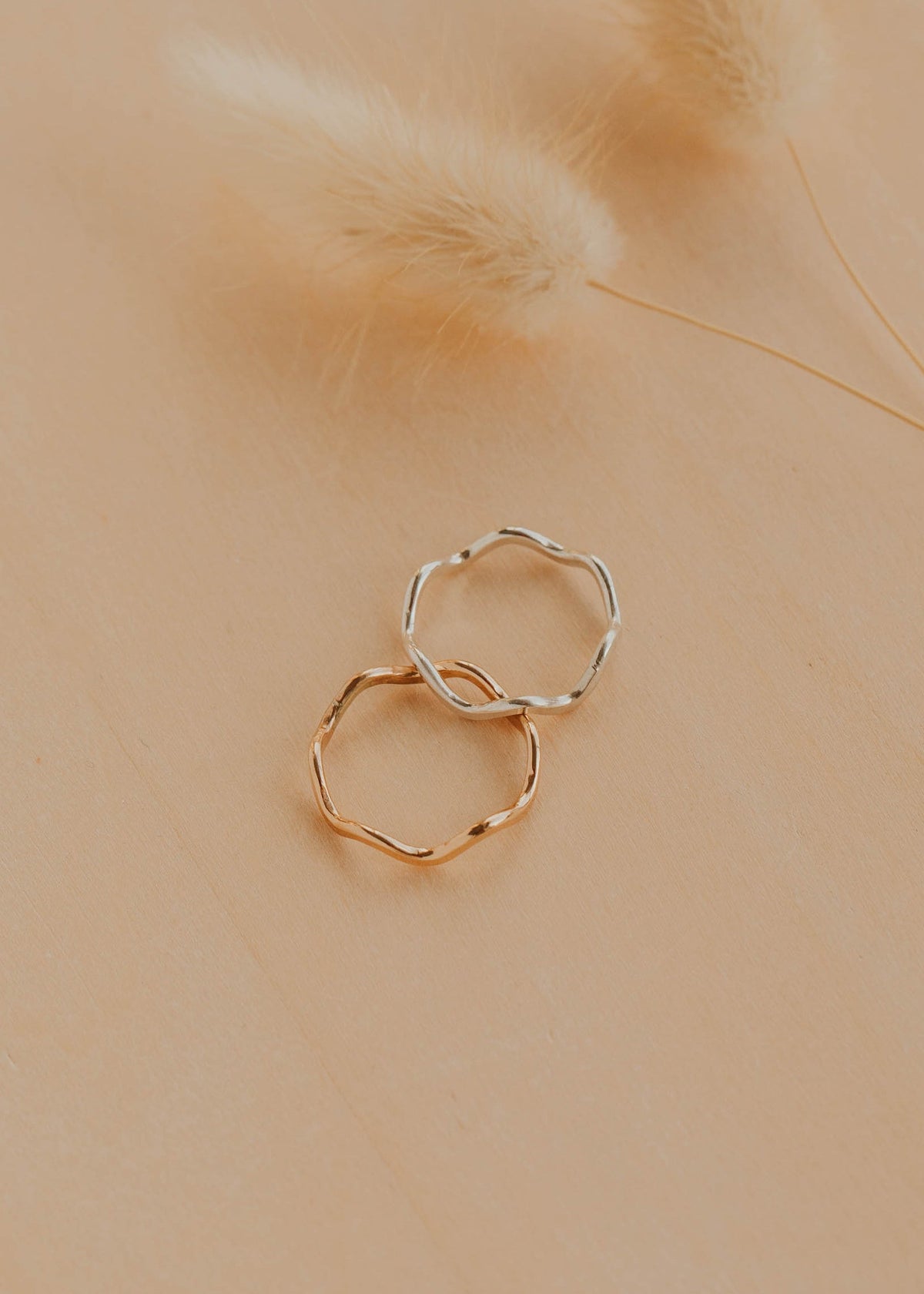 Two gold rings on a beige surface with dried grass.