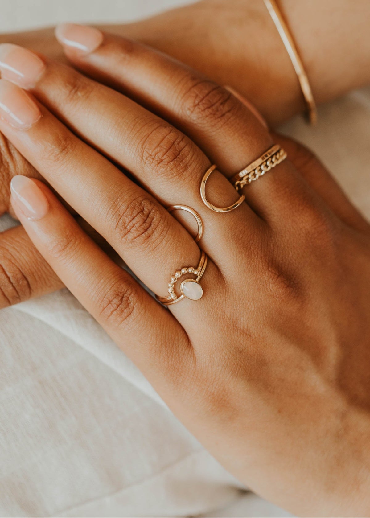 Close-up of hands wearing gold rings on a neutral background