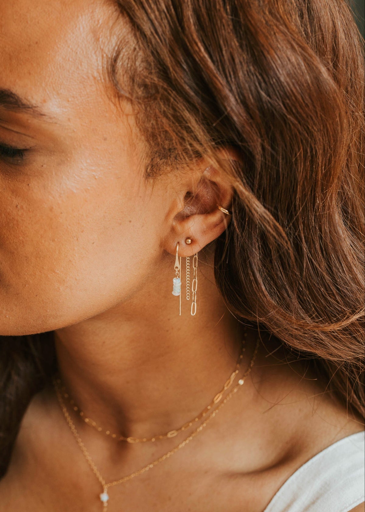 Close-up of a woman wearing gold earrings and necklaces with a neutral background