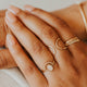 Close-up of hands wearing gold rings on a neutral background