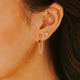 Close-up of a person wearing gold hoop earrings with a blurred background