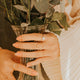 Person holding a clear vase with flowers, wearing a beige sweater.