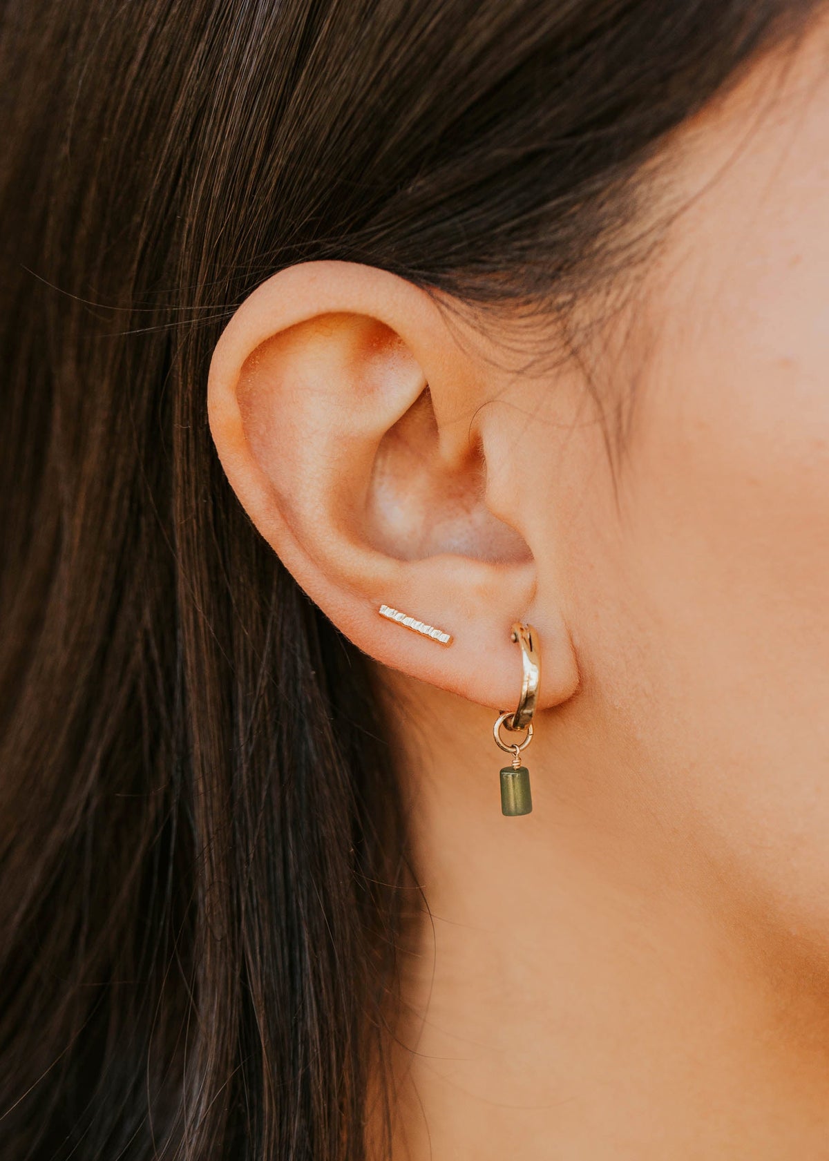Close-up of an ear wearing a gold hoop earring with a green gemstone.