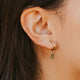 Close-up of an ear wearing a gold hoop earring with a small green gemstone.