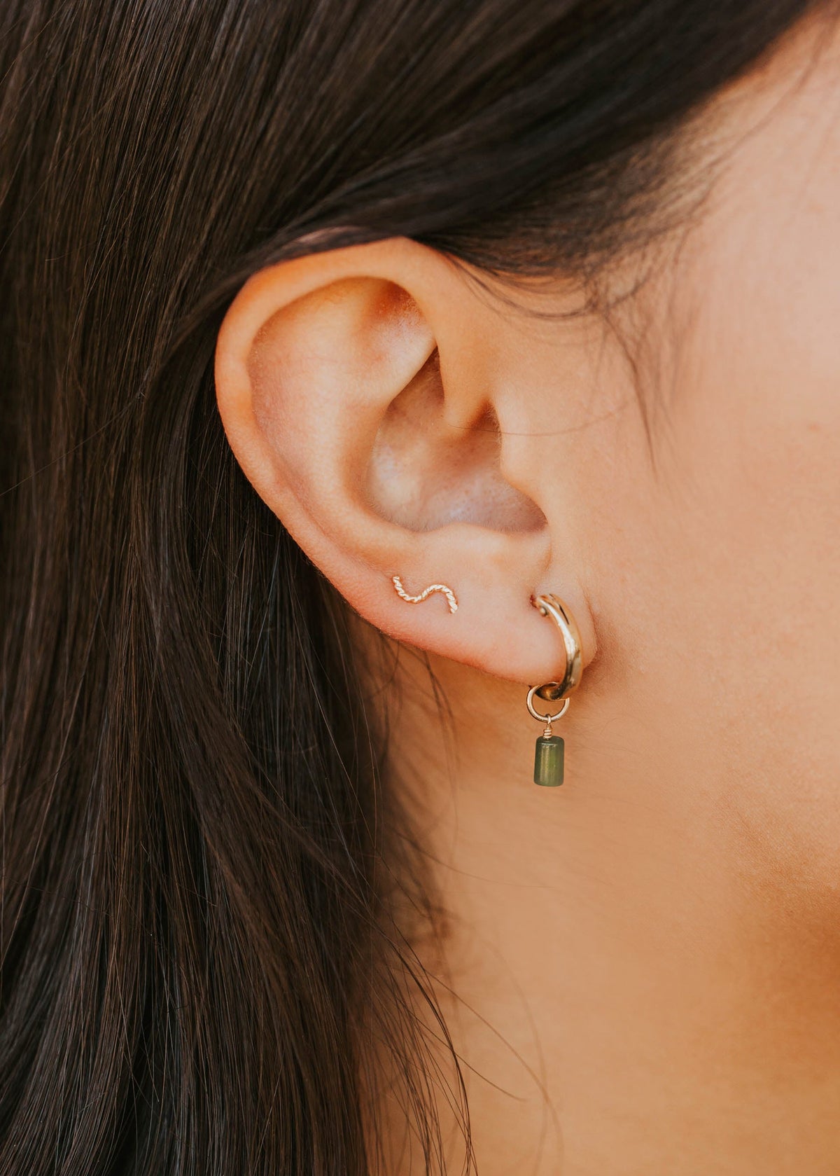 Close-up of an ear wearing a gold hoop earring with a small green gemstone.
