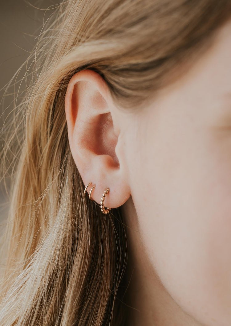 Beaded hoop earrings styled with a double up post to create a fake double piercing creating an earring stack shown in 14k gold fill.