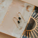 Gold earrings with black beads on a decorative stone surface