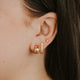 Close-up of an ear wearing gold hoop earrings with a blurred background