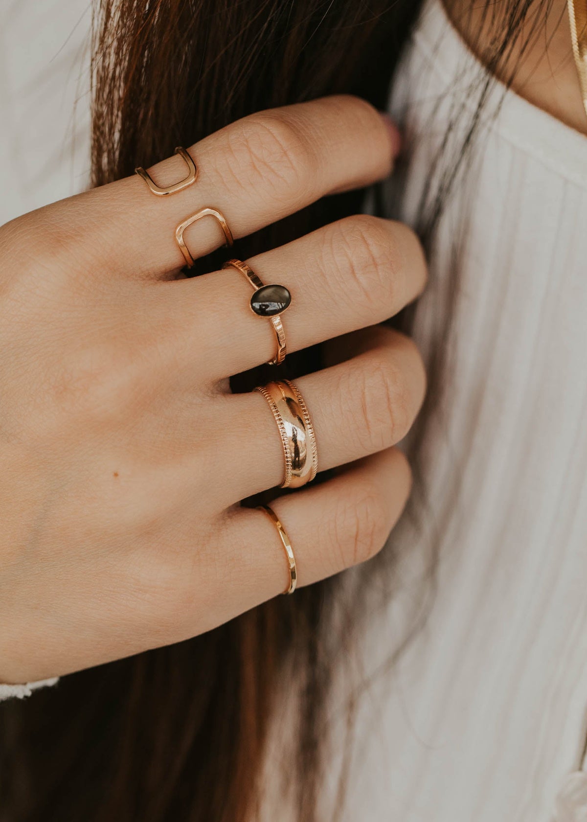 Close-up of a hand wearing multiple gold rings with a blurred background