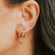 Close-up of an ear wearing gold hoop earrings with small gemstones.