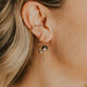 Close-up of an ear wearing a gold earring with a small round pendant.