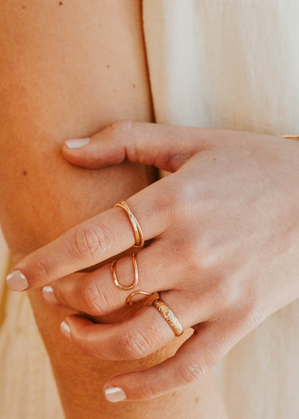 Close-up of a hand with gold rings and bracelet on a neutral background