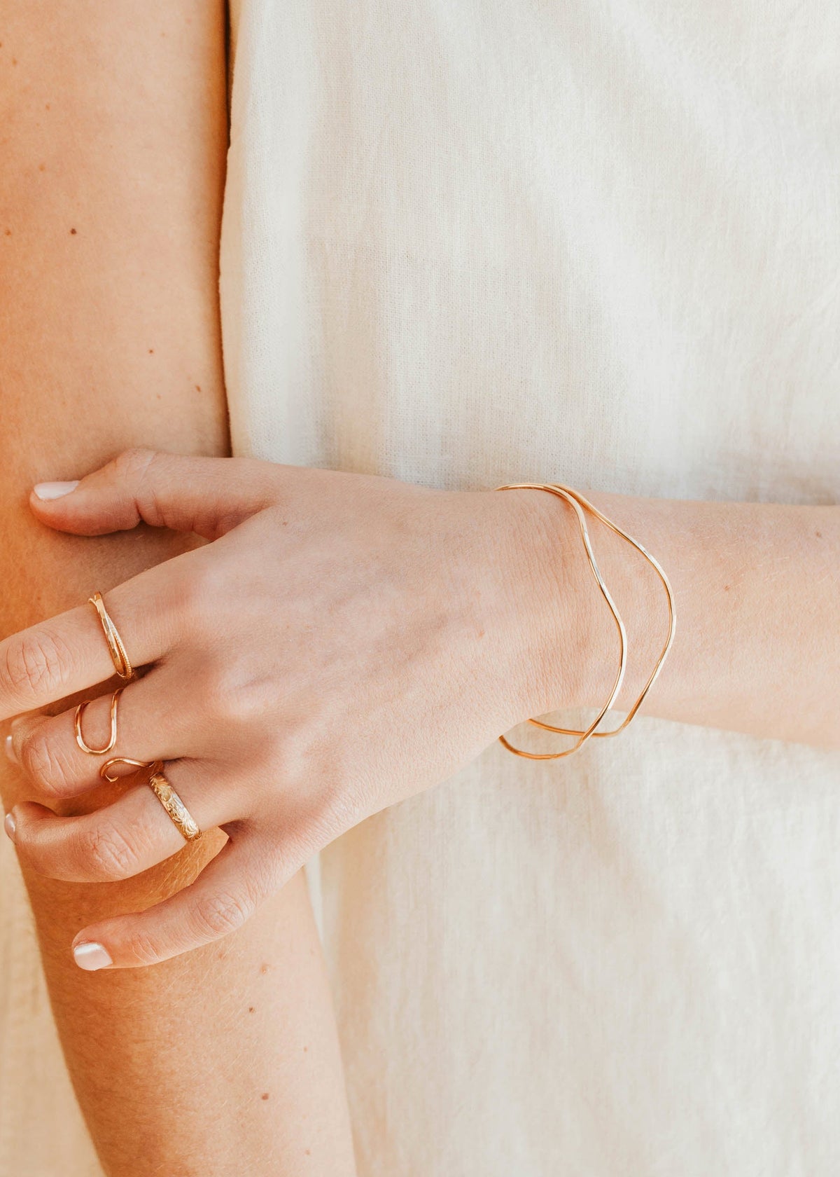 Close-up of a person's arm with gold jewelry including a bracelet and rings.