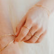 Close-up of hands wearing gold bracelets and rings on a neutral background
