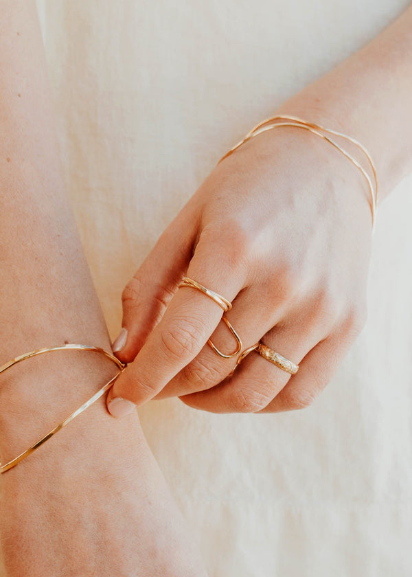 Close-up of hands wearing gold bracelets and rings on a neutral background