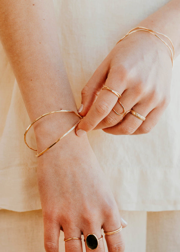 Close-up of hands wearing gold bracelets and rings on a neutral background
