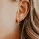 Close-up of an ear with gold earrings against a neutral background
