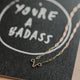 you're a badass card with uterus necklace flat lay