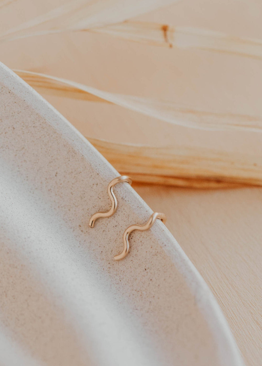14k gold fill wavy ear climber earrings by Hello Adorn resting on a speckled ceramic dish