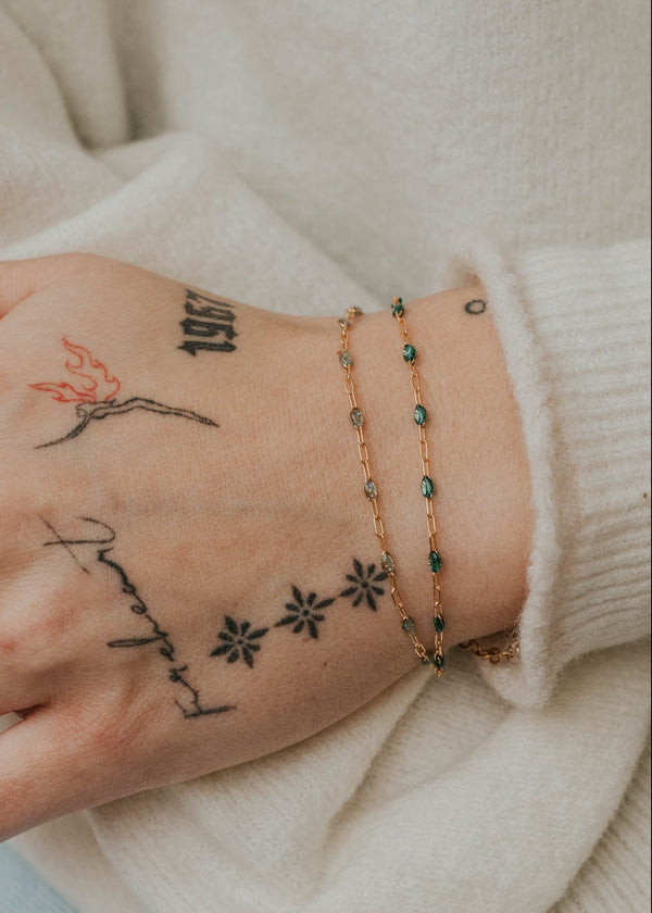 Hand with tattoos and bracelets against a light background