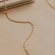 Gold chain necklace on a beige surface with a book in the background