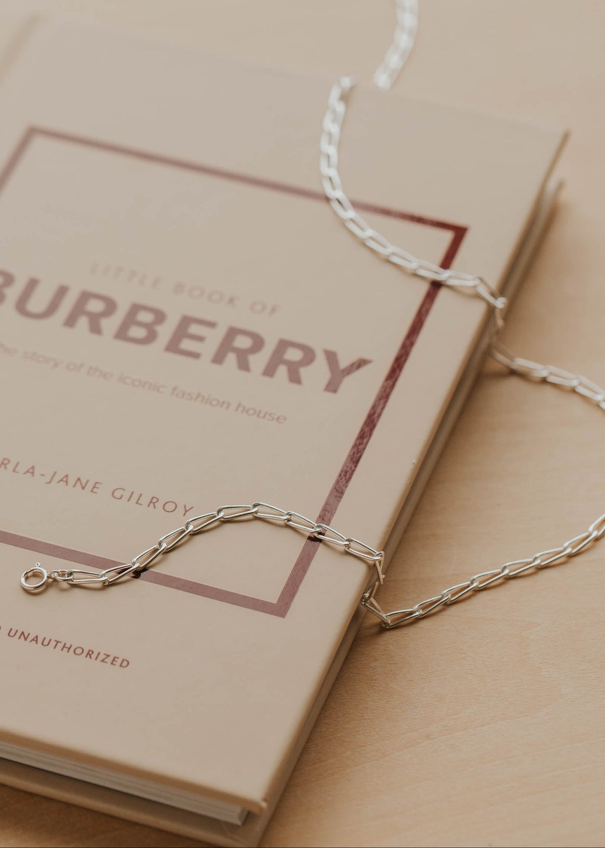 Gold necklace on a beige surface with a Burberry book in the background