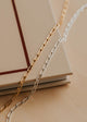 Gold and silver chain necklaces on a beige surface with a book in the background