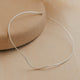 Silver necklace cuff on a beige stone surface