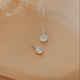 Pair of opal pendants, one silver and one gold, on a beige surface with feathers