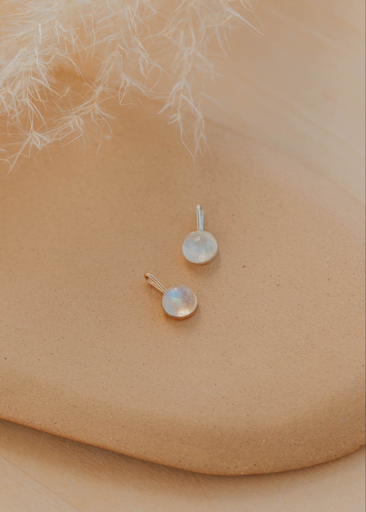 Pair of opal pendants, one silver and one gold, on a beige surface with feathers