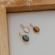 Three gold pendant necklaces with gemstones on a white surface with a wooden frame.