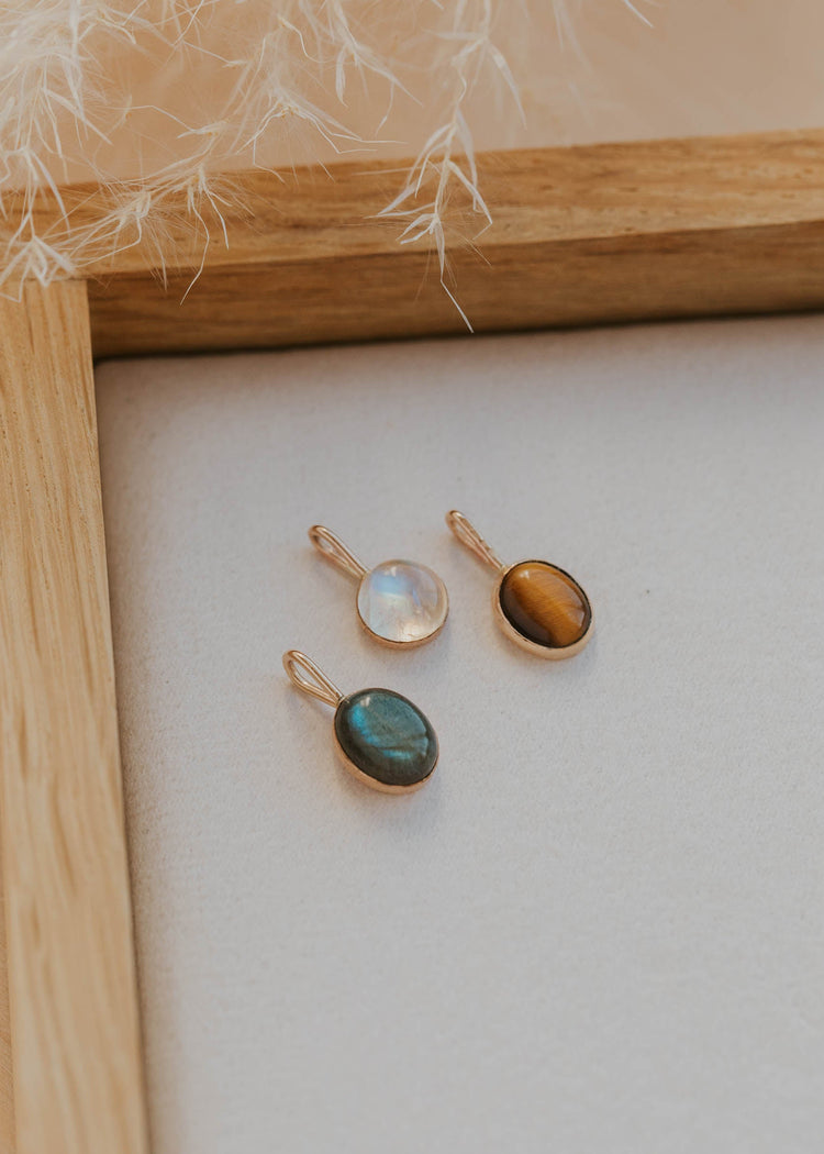 Three gold pendant necklaces with gemstones on a white surface with a wooden frame.