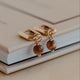 Gold earrings with brown beads on a beige surface