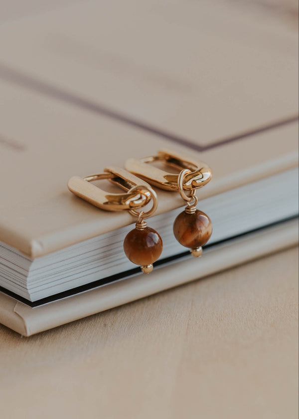 Gold earrings with brown beads on a beige surface