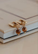 Gold earrings with brown beads on a beige surface