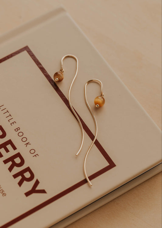 Gold earrings with a small round bead on a book