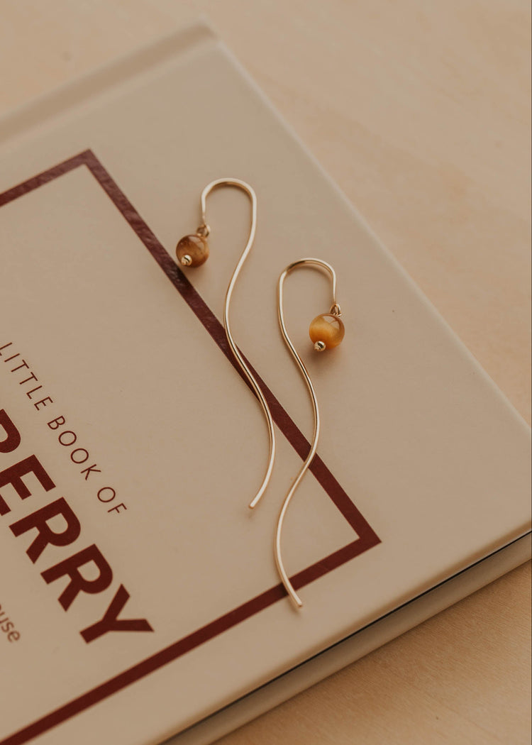 Gold earrings with a small round bead on a book