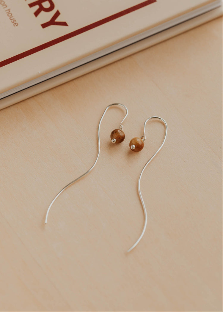 Pair of earrings with brown beads on a beige surface with a book in the background