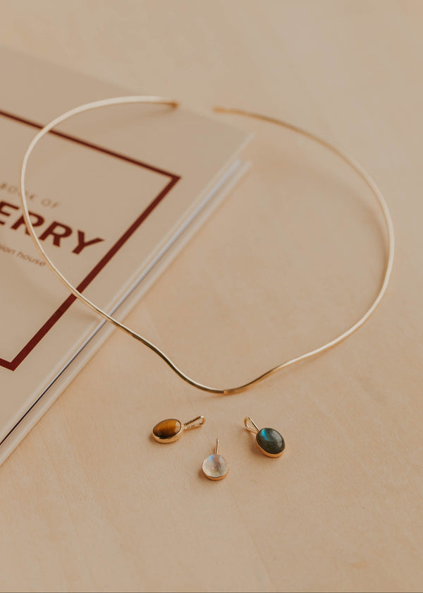 Gold necklace with three pendants on a beige surface