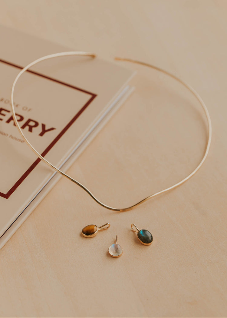 Gold necklace with three pendants on a beige surface